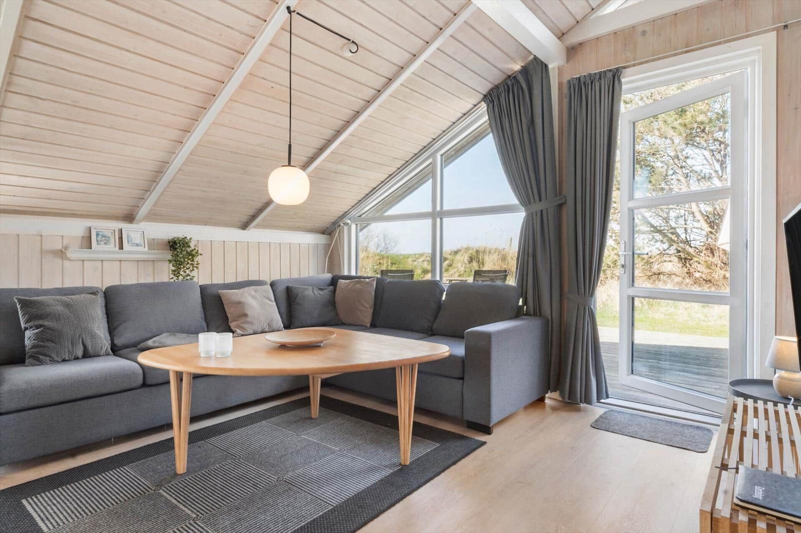 Wohnzimmer mit Sofa, Tisch und großem Fenster. Holzdecke und Boden.