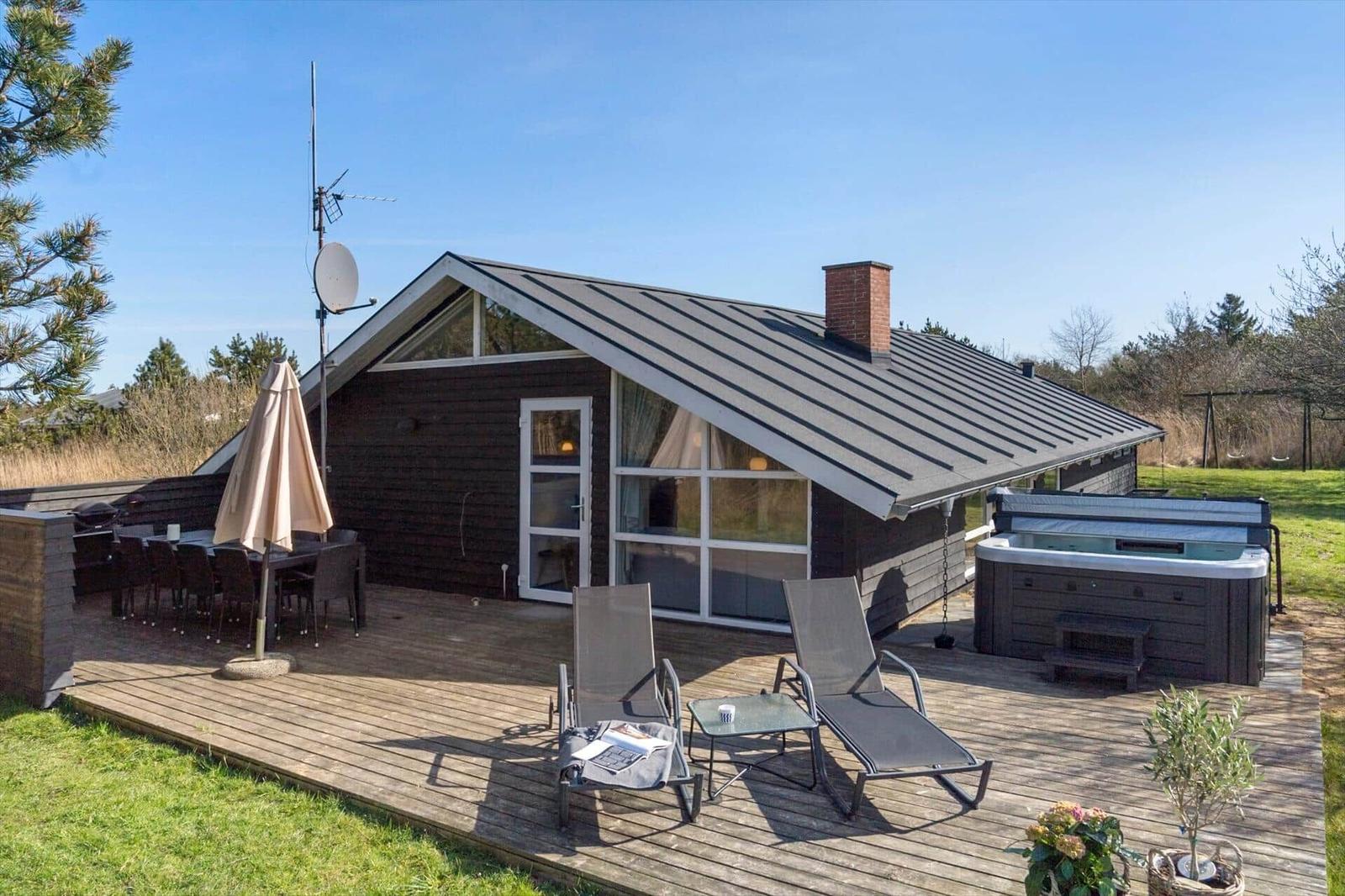 Haus mit Terrasse, Liegen, Whirlpool und Grillplatz im Freien.