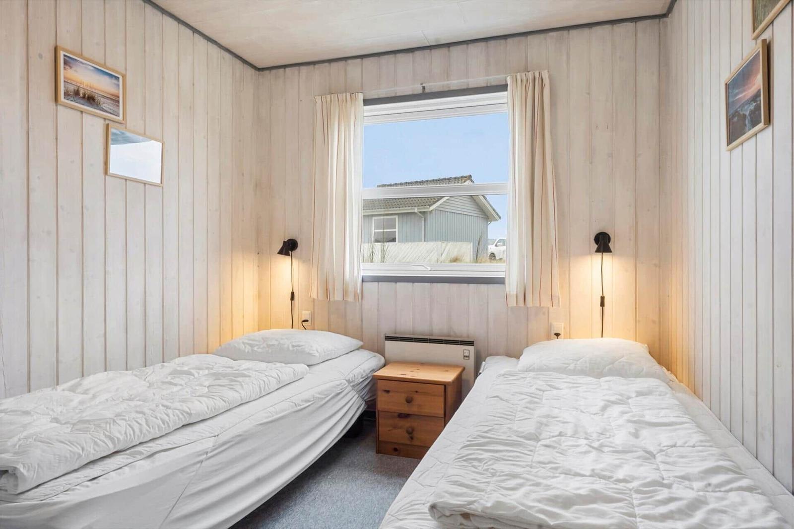 Zwei Betten mit weißen Bettwäsche, Holzwand und Fenster mit Blick auf Haus.