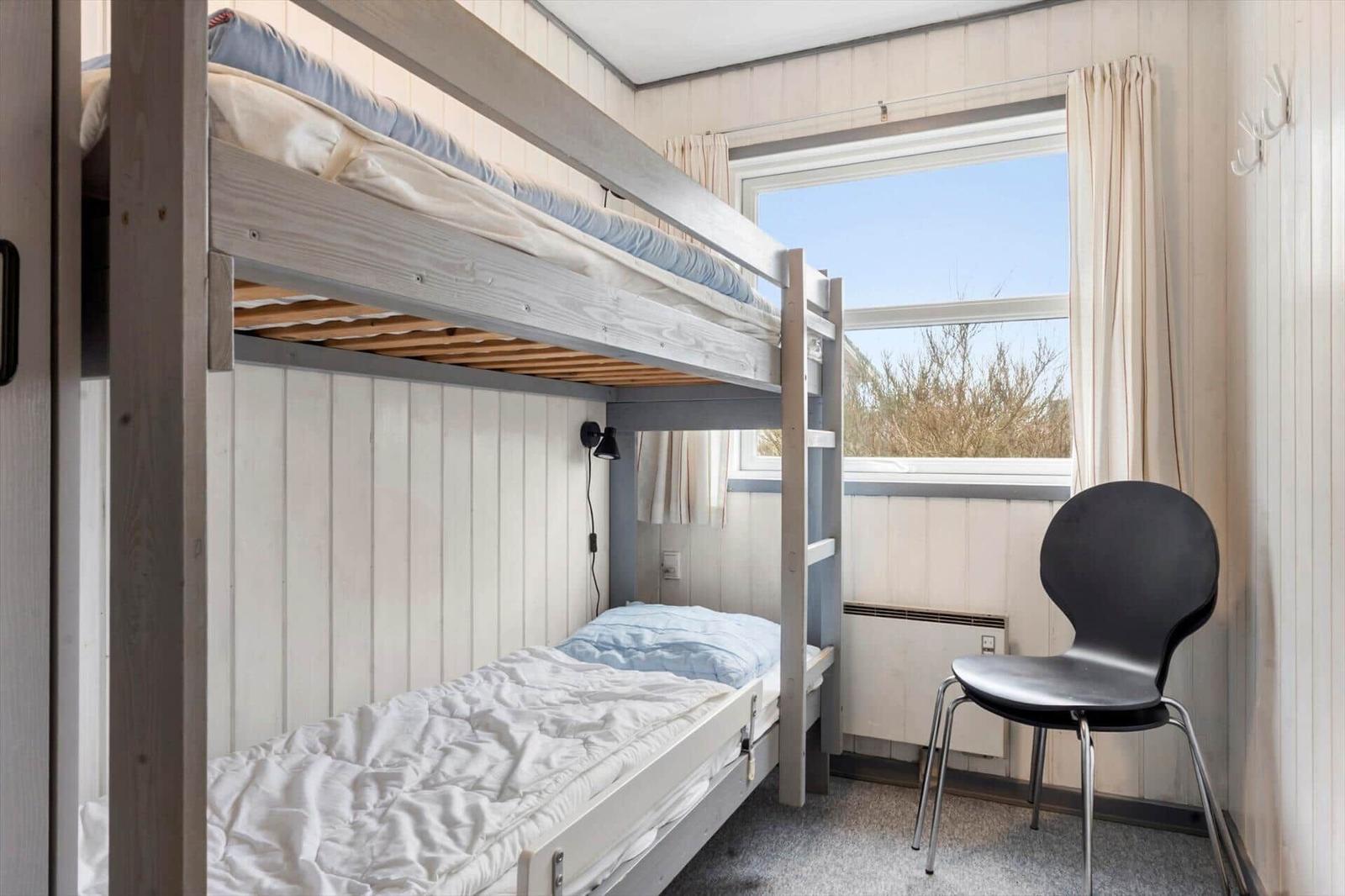Zimmer mit Doppelstockbett, Stuhl und Fenster mit Blick auf Bäume.