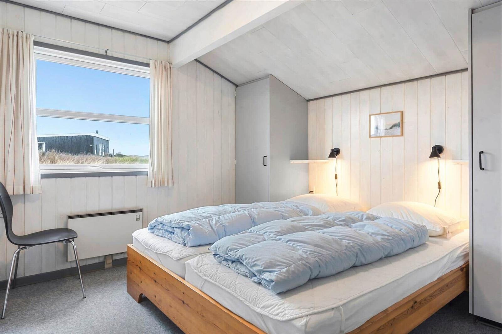 Schlafzimmer mit Bett, Fenster und Kleiderschrank. Holzboden und Wandverkleidung.