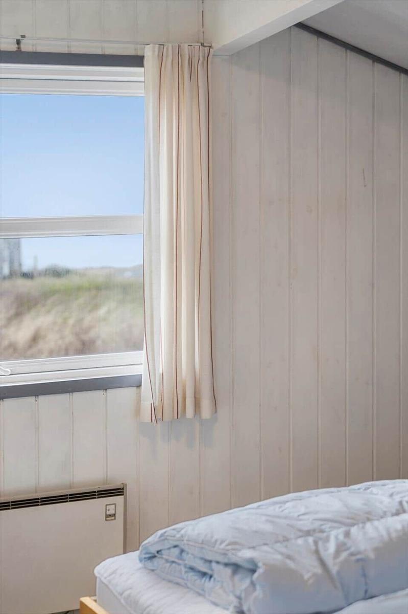 Schlafzimmer mit Bett, Fenster und Holzwand. Vorhang und Heizkörper sind sichtbar.