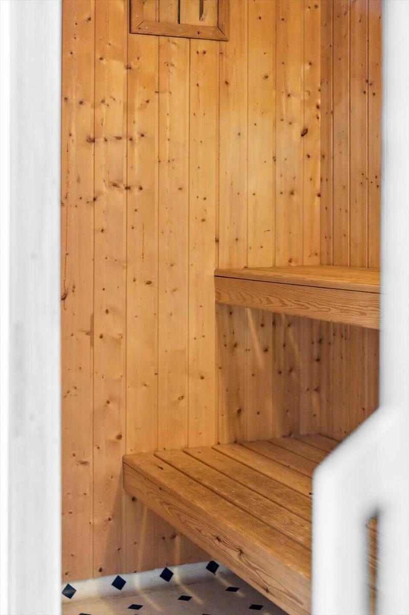 Sauna mit Holzwänden und zwei Bänken. Boden mit schwarz-weißem Mosaik.