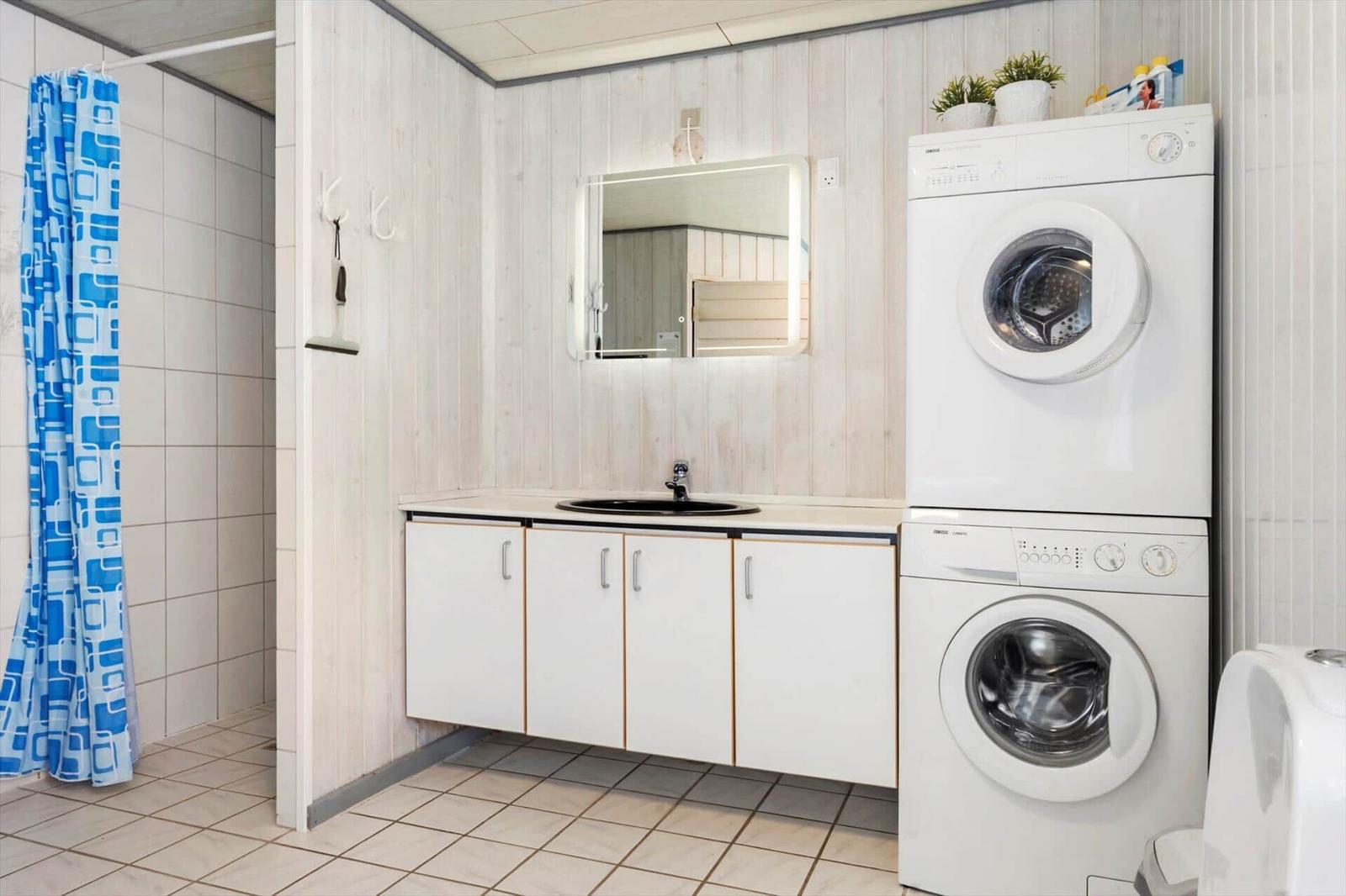 Badezimmer mit Waschmaschine, Spiegel und Dusche mit blauem Vorhang.
