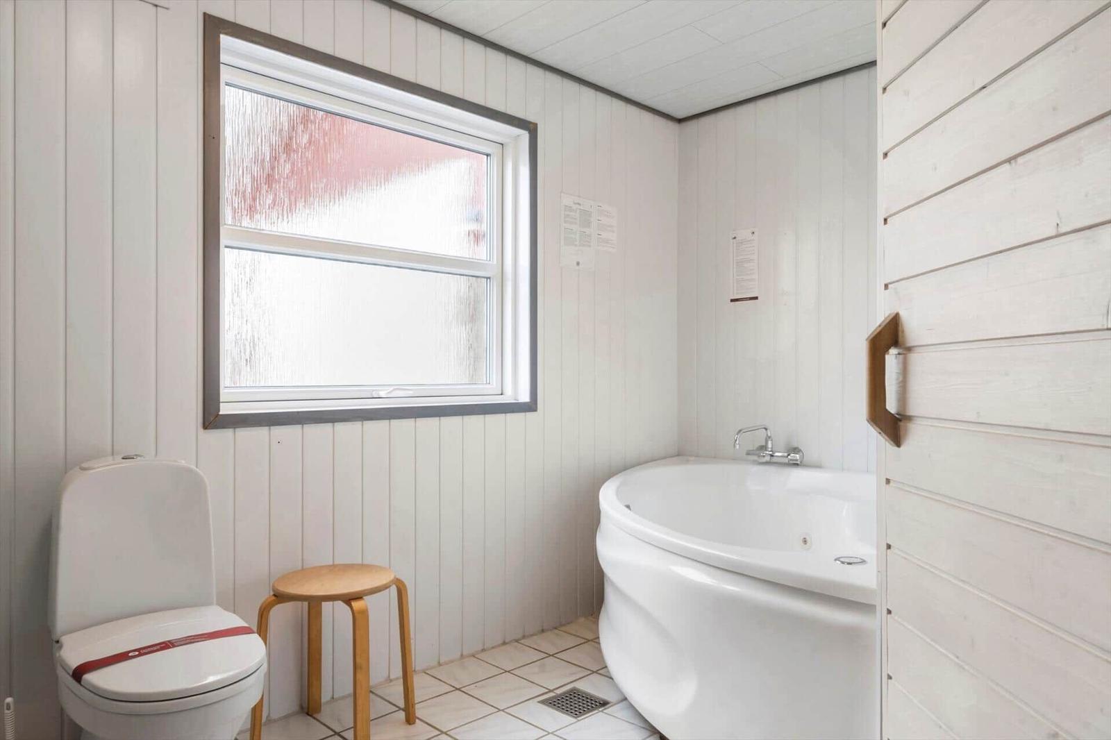 Bad mit Badewanne, Toilette und Fenster mit getöntem Glas.