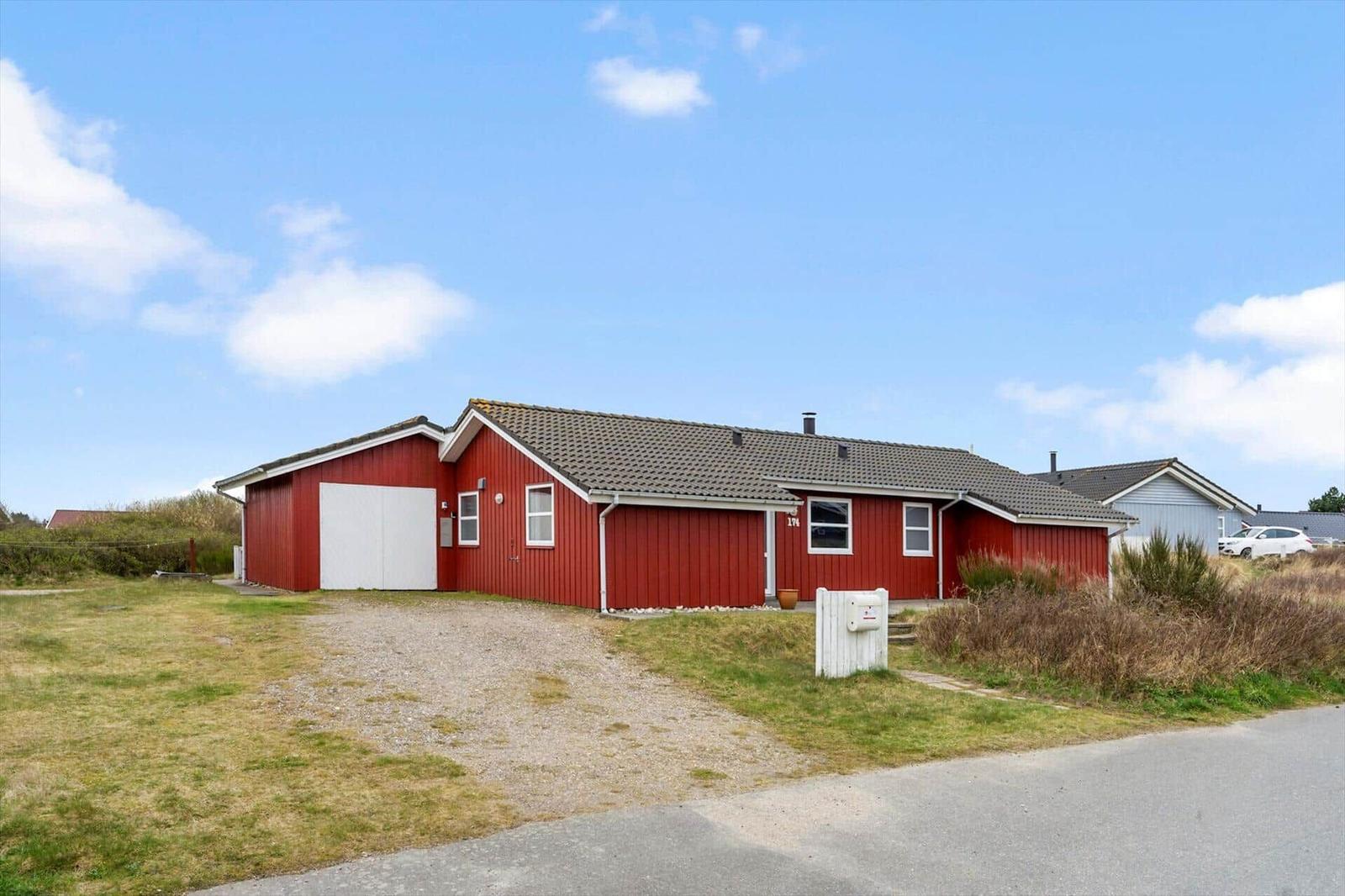 Rotes Ferienhaus mit Garage und Garten unter blauem Himmel.
