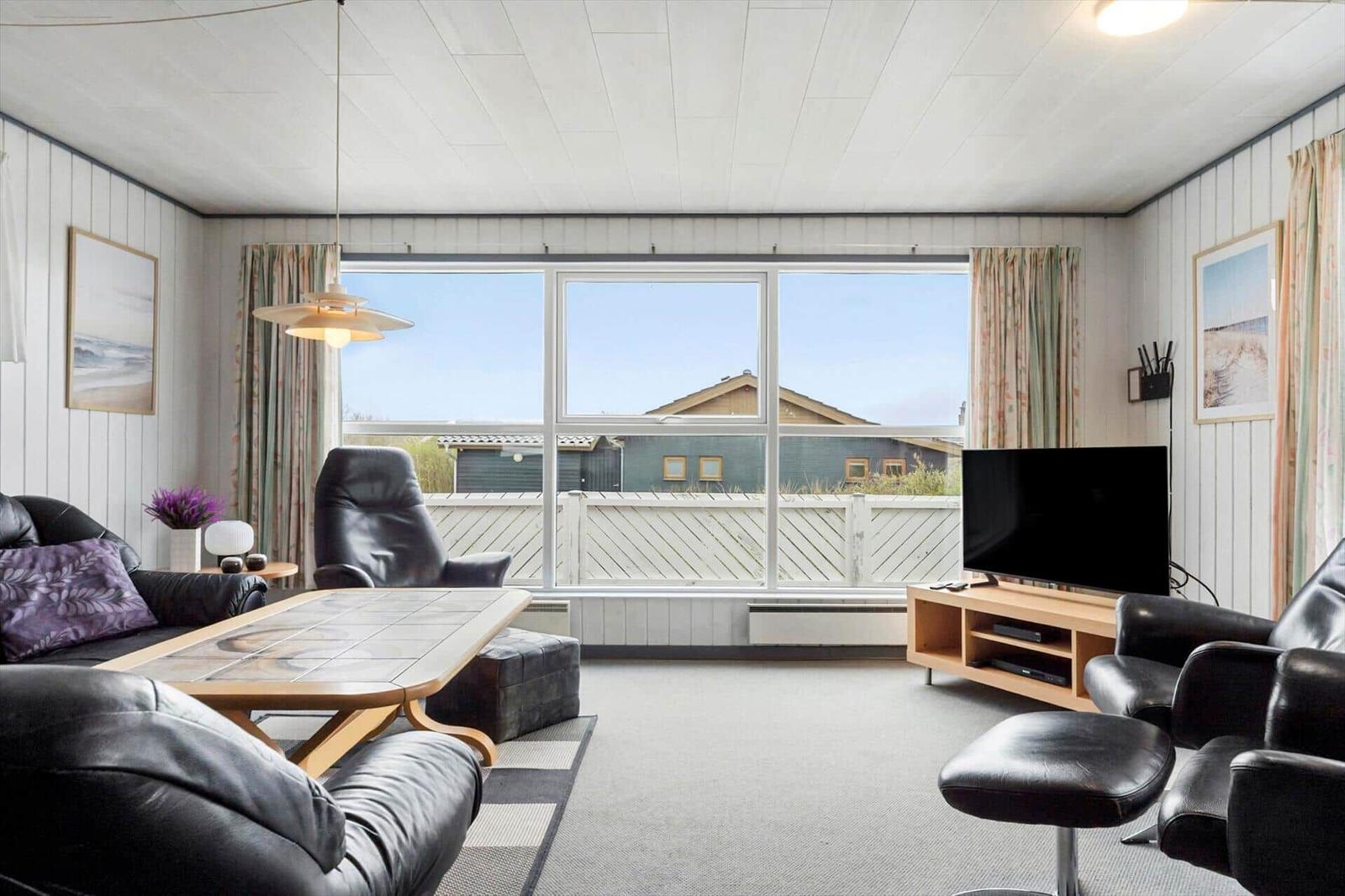 Wohnzimmer mit Sitzgelegenheiten, Fernseher und großem Fensterblick.