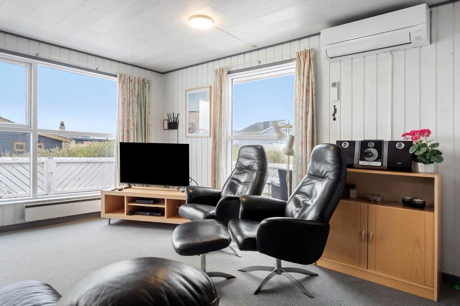 Wohnzimmer mit zwei schwarzen Sesseln, Fernseher und Fenstern mit Blick.