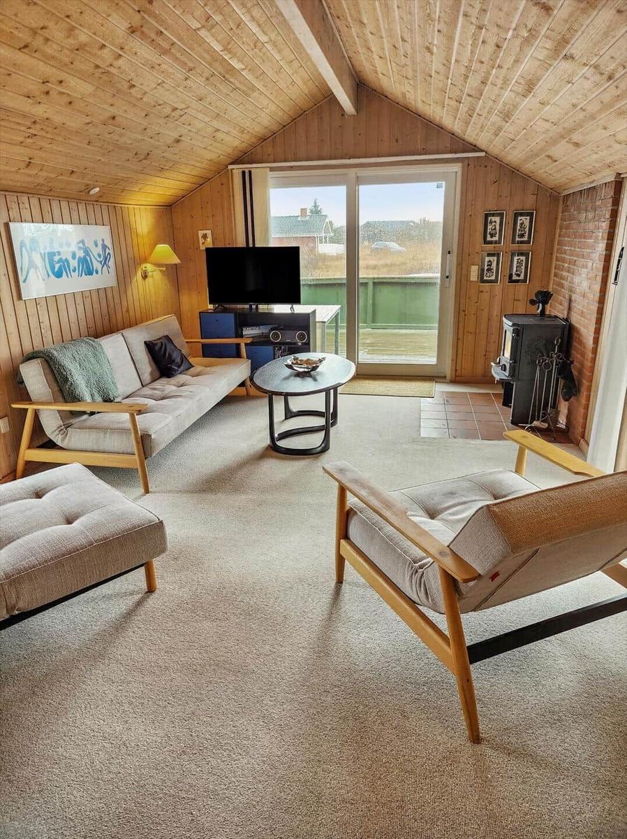 Wohnzimmer mit Sofa, Sessel und TV. Holzwände und Dach. Terrasse mit Blick.
