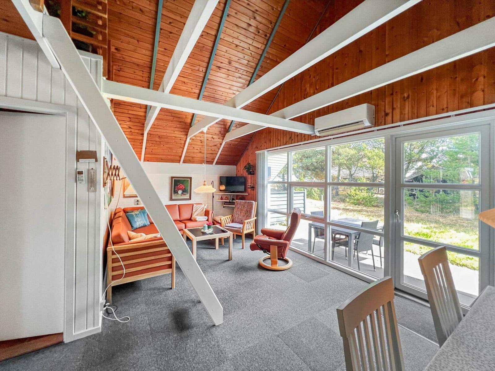 Living room with wooden ceiling, sofa, armchair, and large window to terrace.