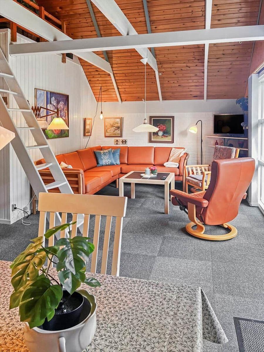 Living area with orange sofa, wooden ceiling, and staircase.