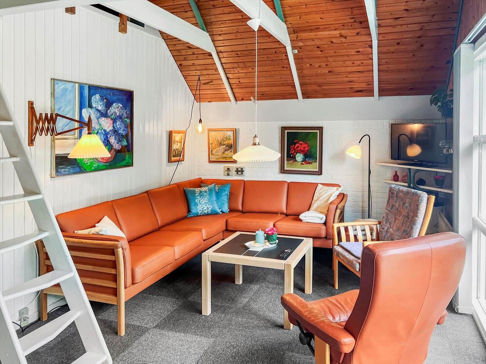 Living room with orange sofa, wooden ceiling, and wall paintings.