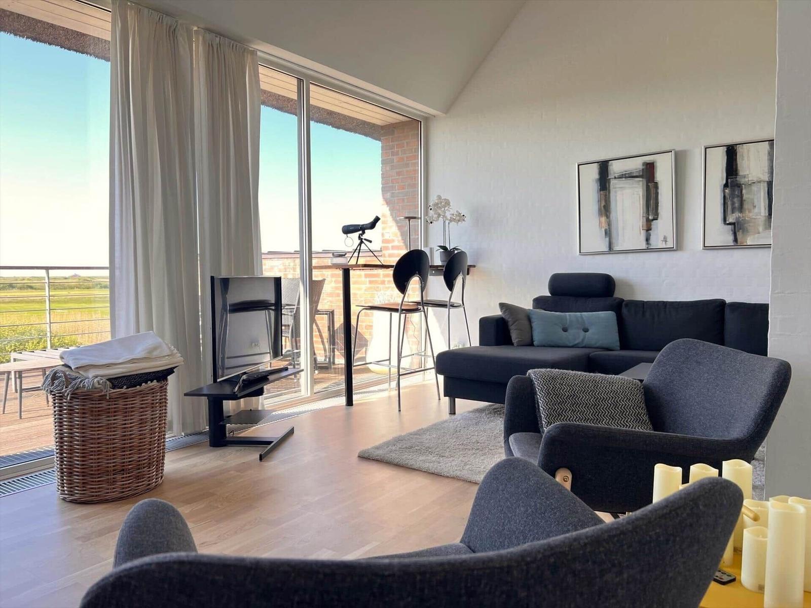 Living room with sofa, chairs, and balcony view. TV, pictures, and telescope visible.