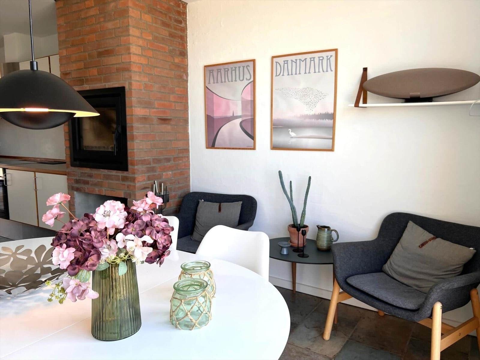 Dining area with table, chairs, and flowers. Wall art and armchairs in the background.