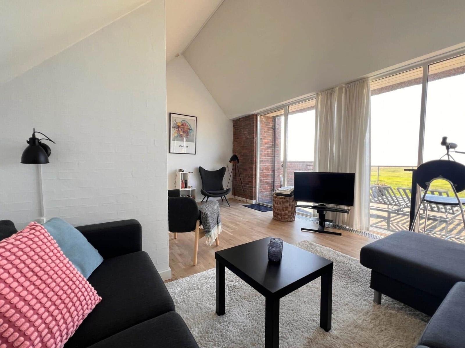 Living room with sofa, coffee table, and TV. Large windows with balcony view.