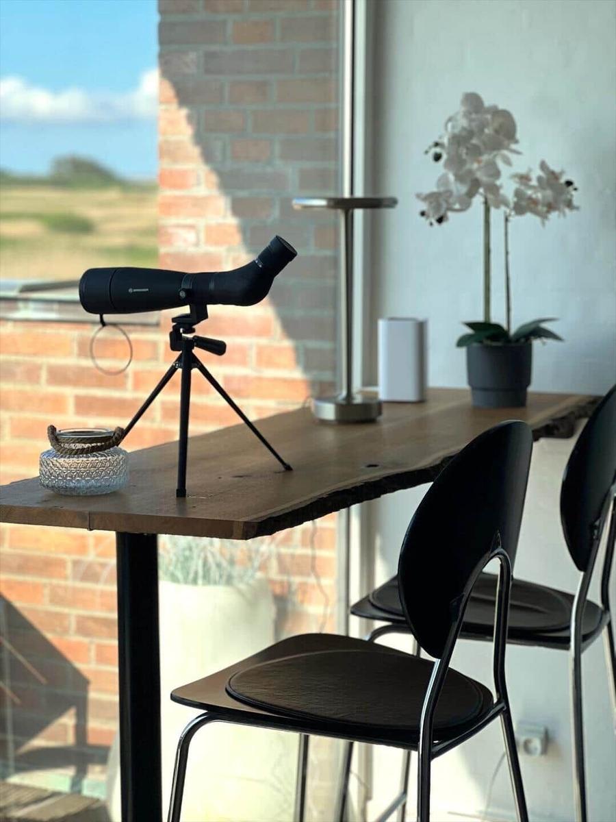 A table with binoculars, chair, and plant by window with view of landscape.