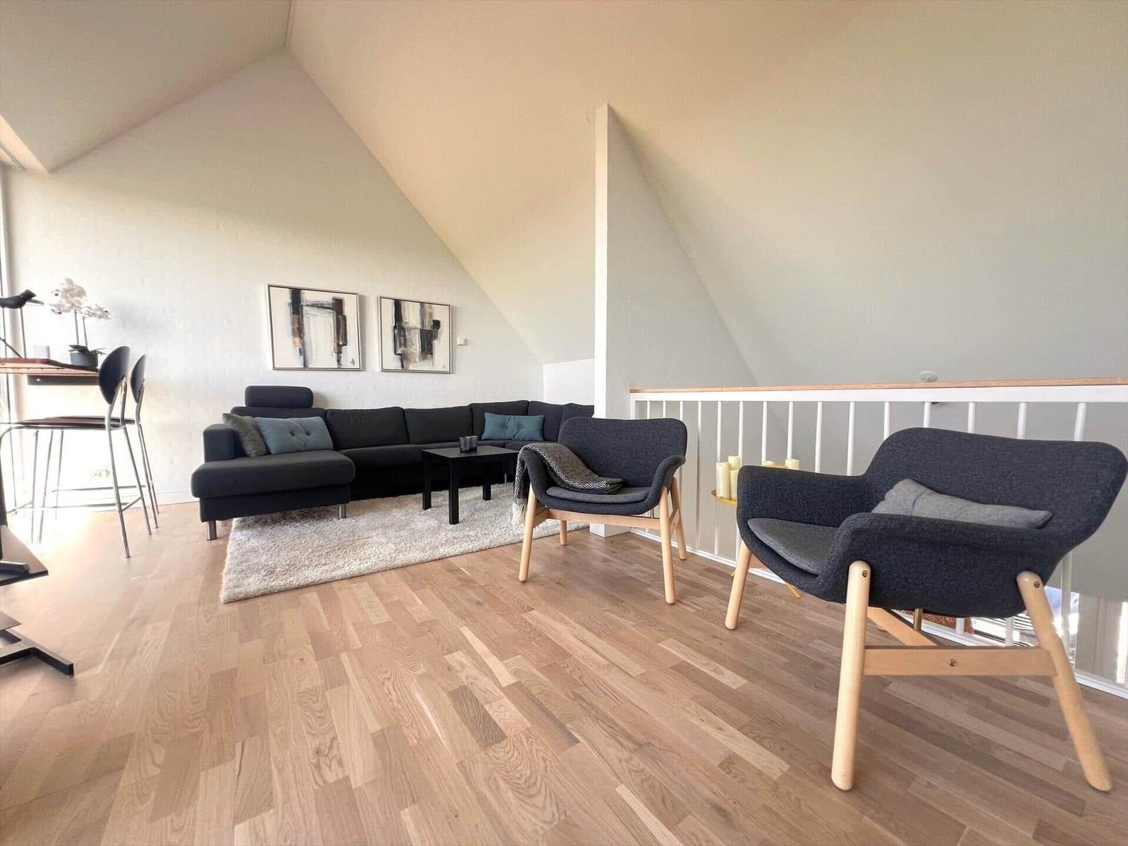 Living room with sofa, two armchairs, and wooden floor under sloped walls.