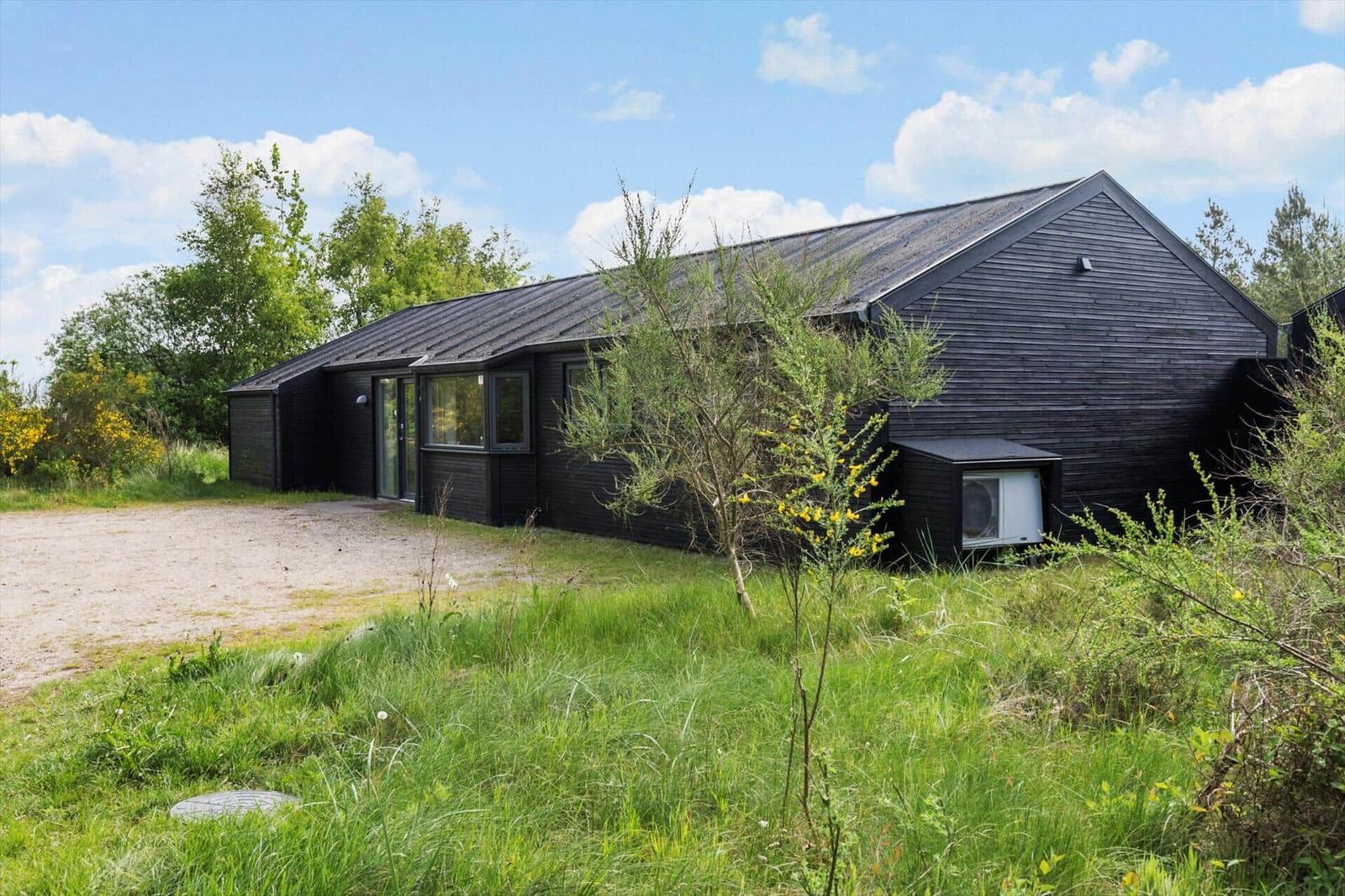 Schwarzes Holzhaus mit Dach und Fenstern in grüner Umgebung unter blauem Himmel.