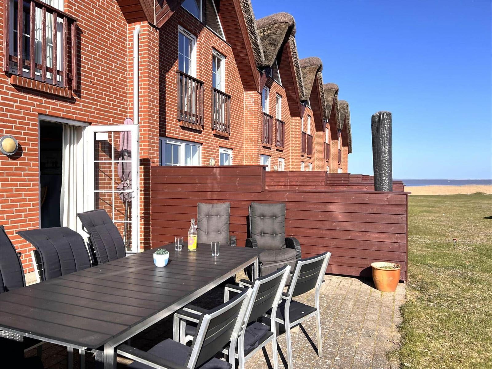 Terrasse mit Tisch und Stühlen vor einem roten Backsteinhaus mit Dach aus Stroh.