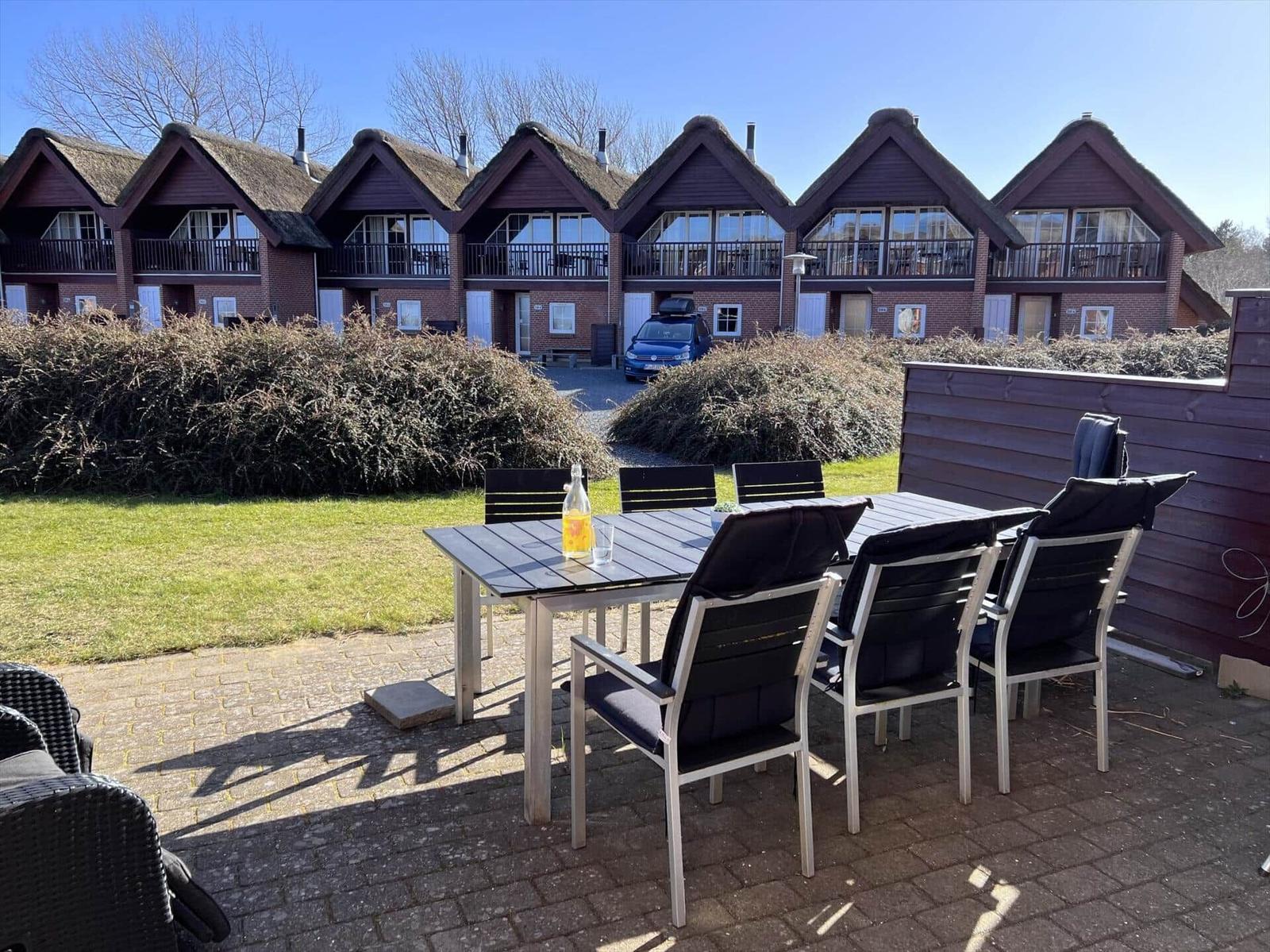 Terrasse mit Tisch und Stühlen. Im Hintergrund stehen mehrere Häuser mit Dächern.