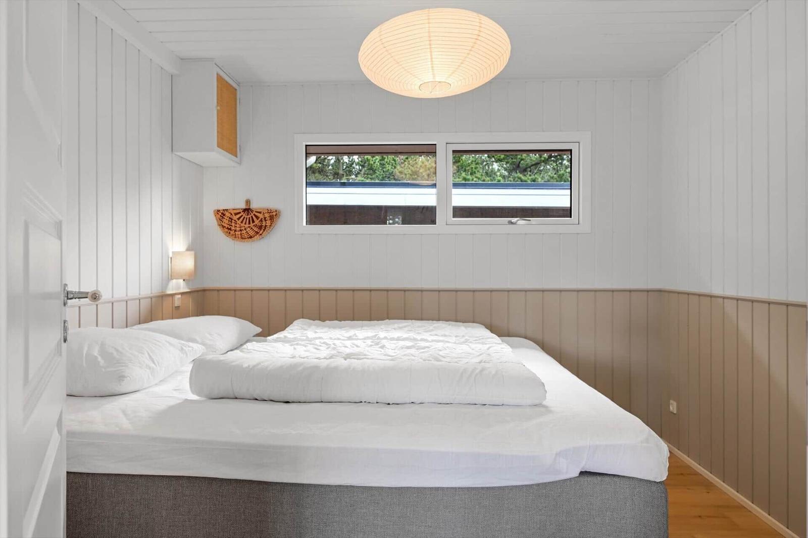 Ein Schlafzimmer mit weißer Wandverkleidung, einem Bett und einem Fenster.