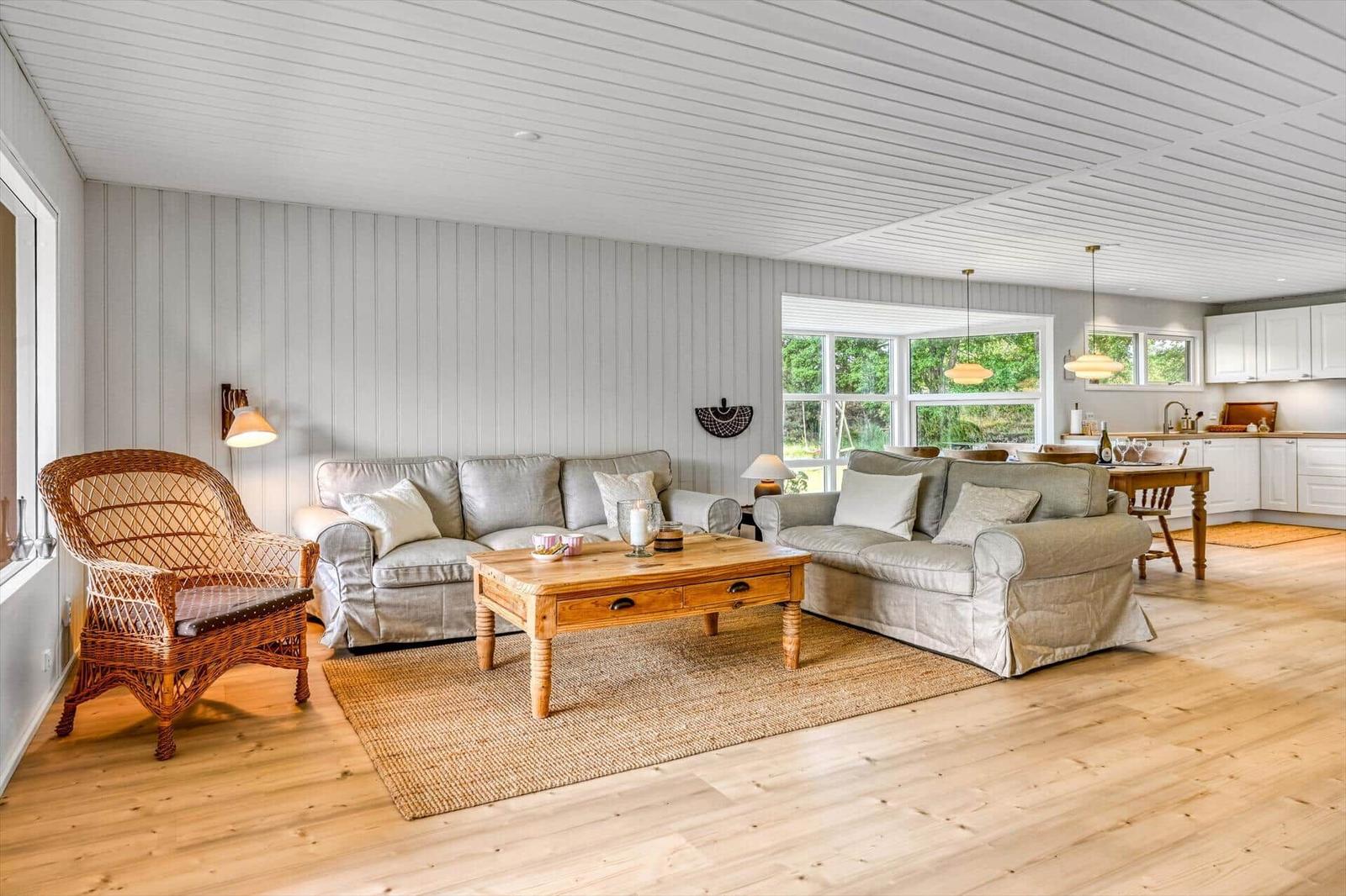 Wohn- und Essbereich mit Holzboden, Sofa, Wickerstuhl und Küchenbereich im Hintergrund.