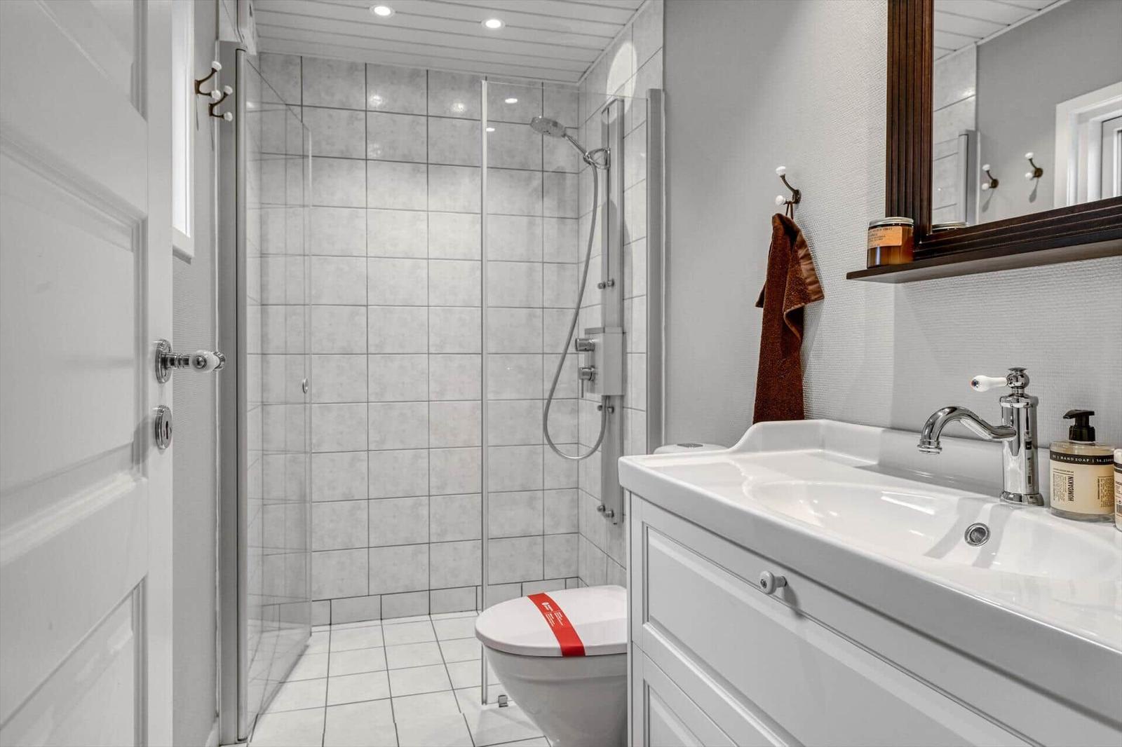 Badezimmer mit Dusche, Waschbecken und Toilette. Weiße Fliesen und Spiegelschrank.