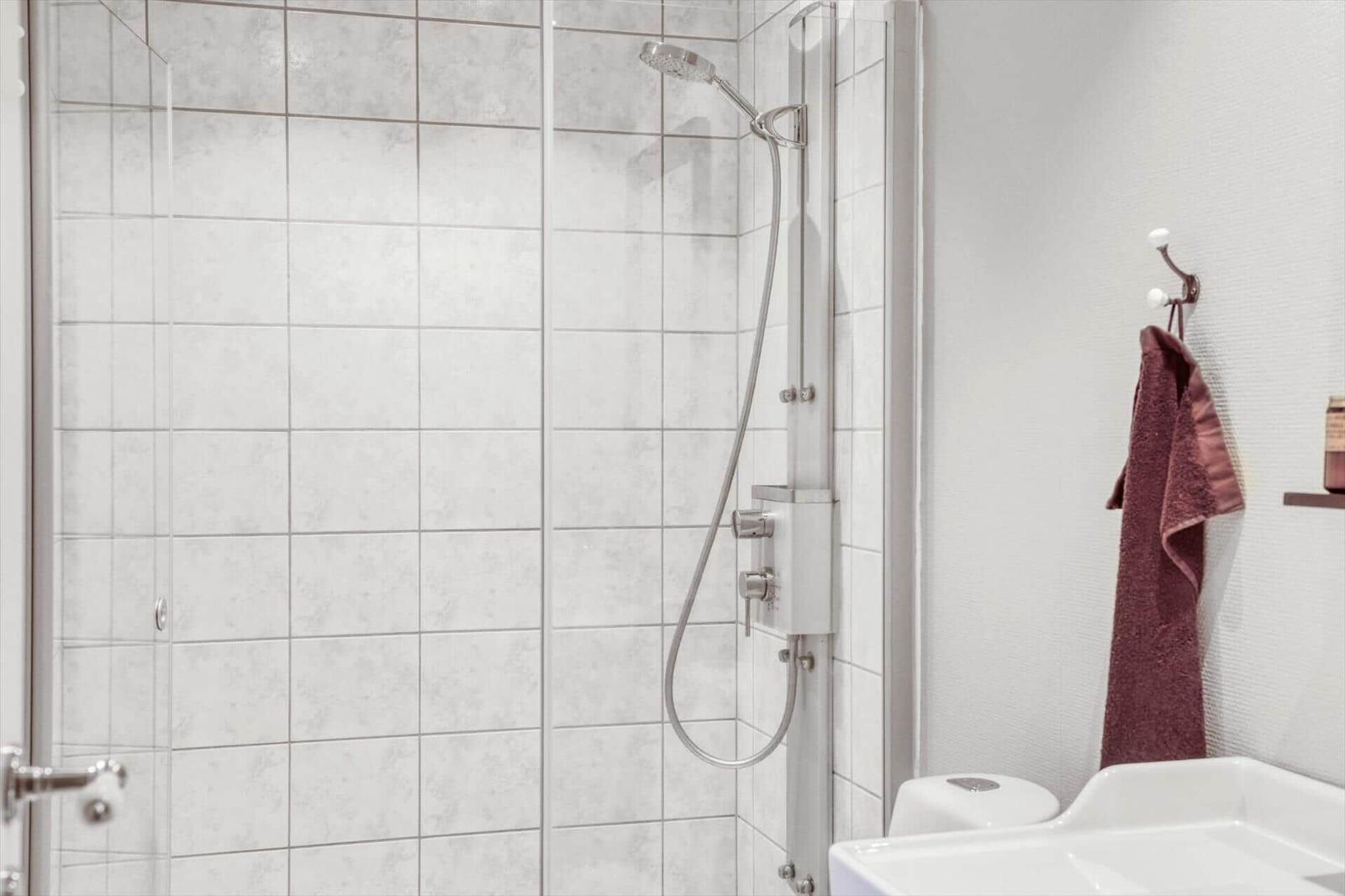 Dusche mit Duschbrause und Handbrause, daneben Toilette und Waschbecken mit Handtuch.