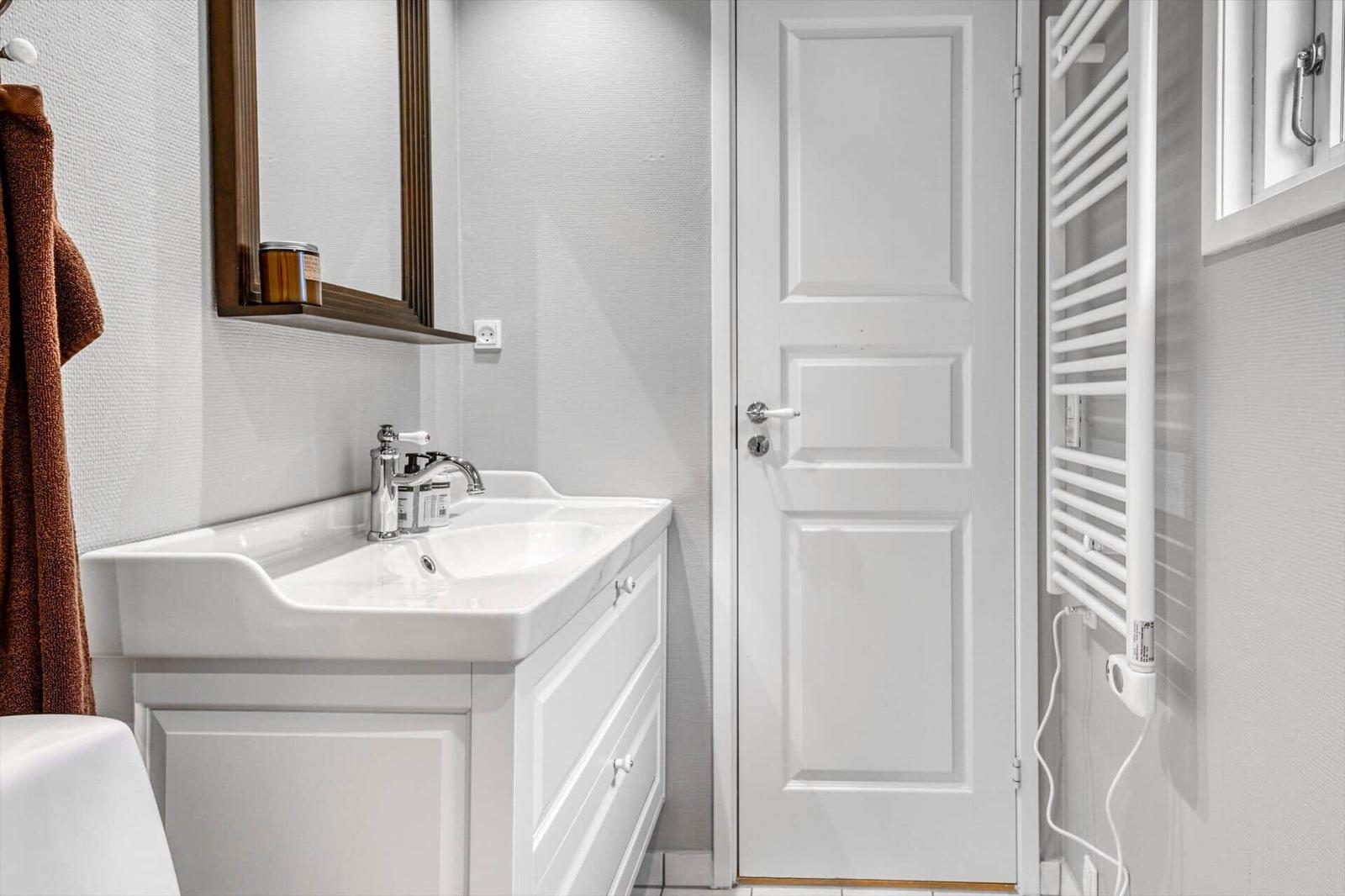 Badezimmer mit Waschbecken, Spiegel, Heizkörper und Tür.