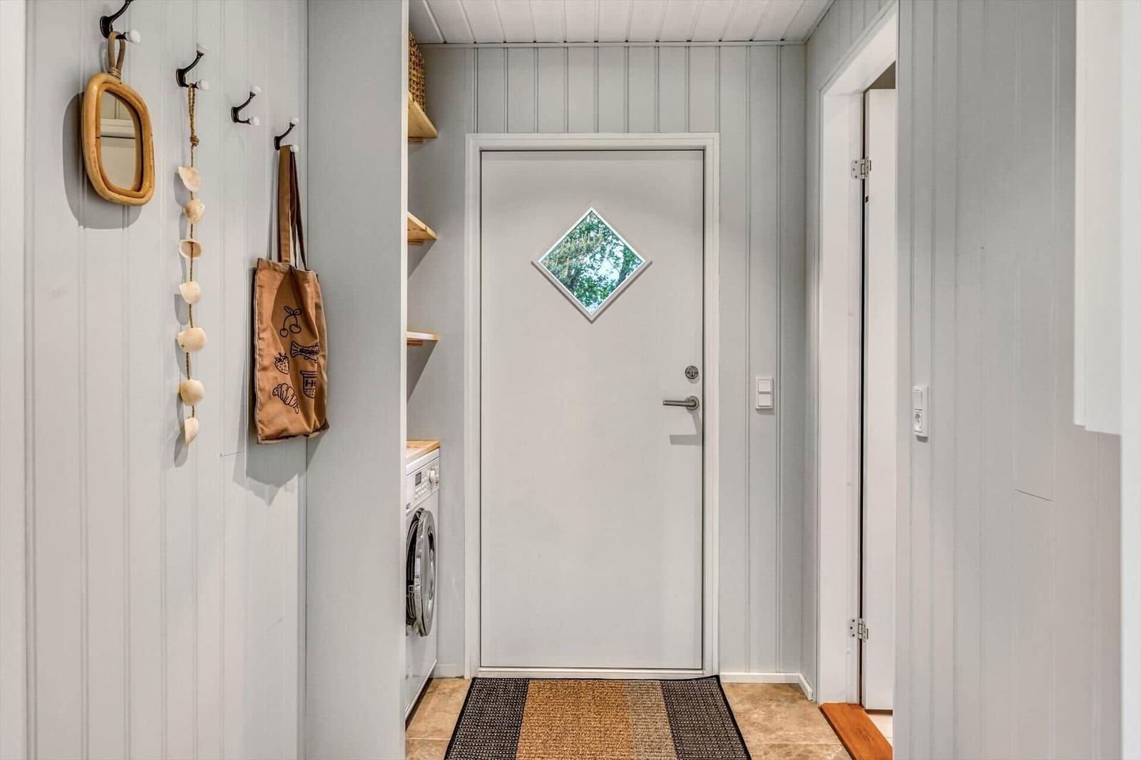 Eingangsbereich mit Waschmaschine und Wandregal. Tür mit Diamantfenster. Holzdielenboden.