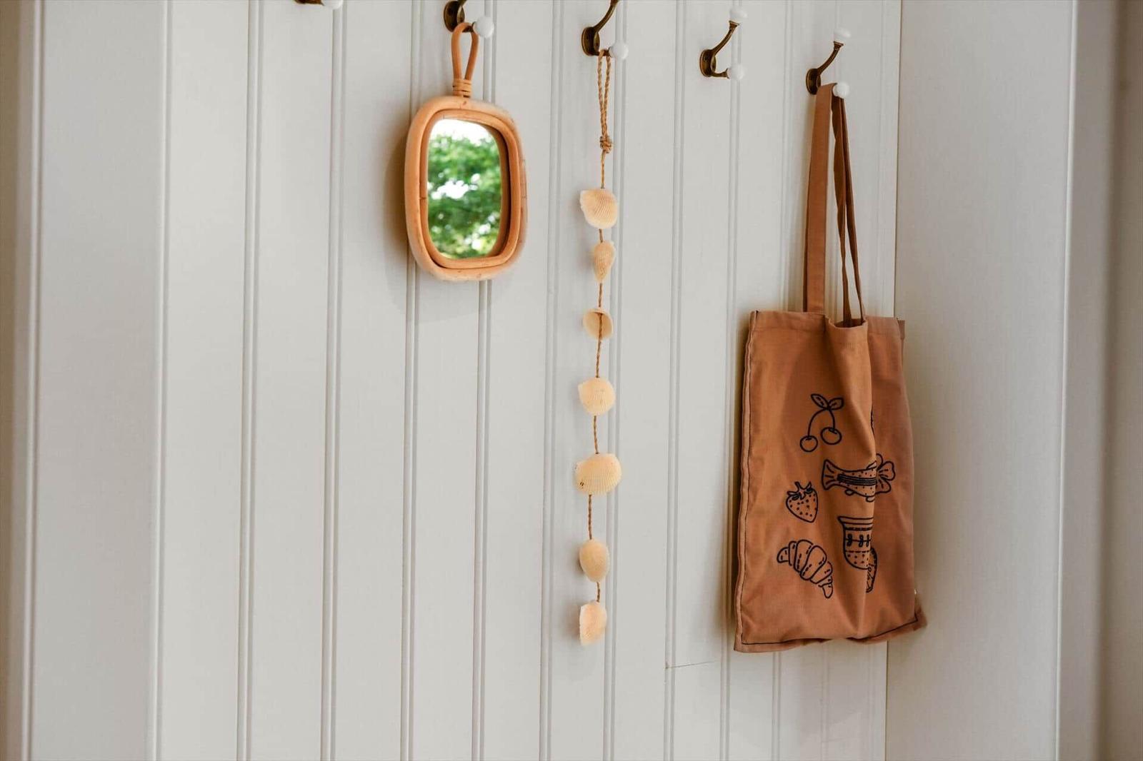 An der Wand hängen ein Spiegel, eine Muschelkette und eine Tasche.