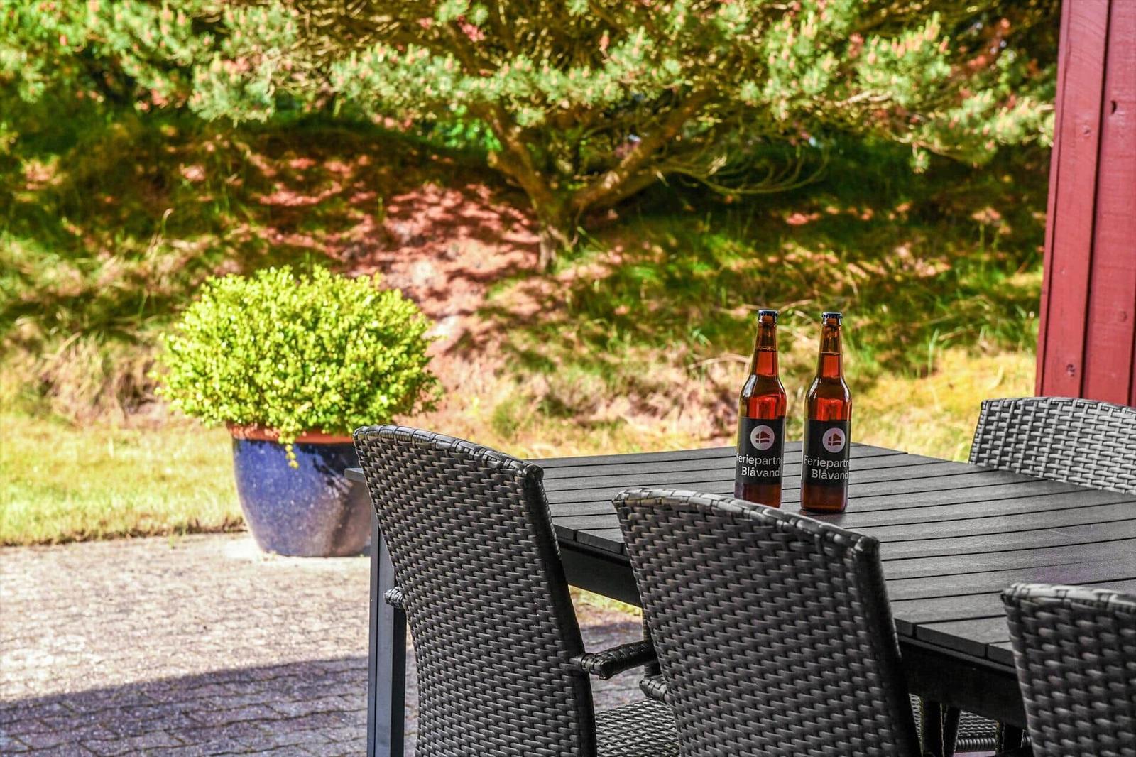 Außenbereich mit Tisch, Stühlen und zwei Flaschen. Hintergrund: Grünflächen und Pflanzen.