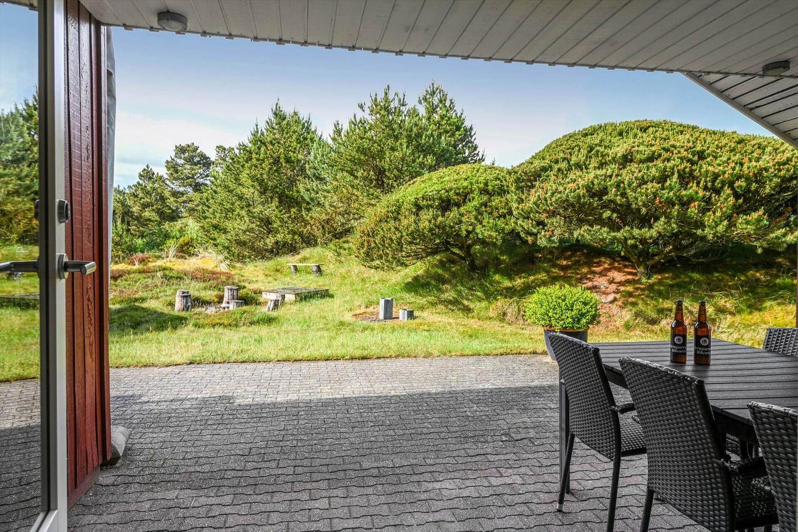 Terrasse mit Tisch und Stühlen, Blick auf grüne Wiese und Bäume.
