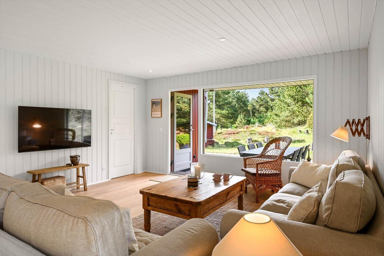 Wohnzimmer mit Sofa, Couchtisch und Fernseher. Durchgang zur Terrasse mit Gartenblick.