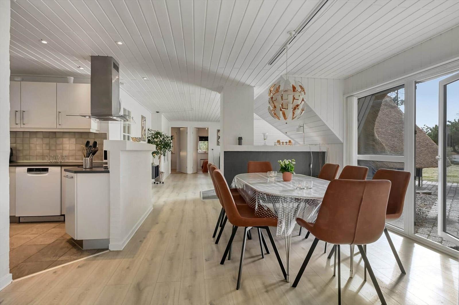 Küche und Essbereich mit Tisch, Stühlen und Glasfront. Holzboden und weißer Deckenverkleidung.