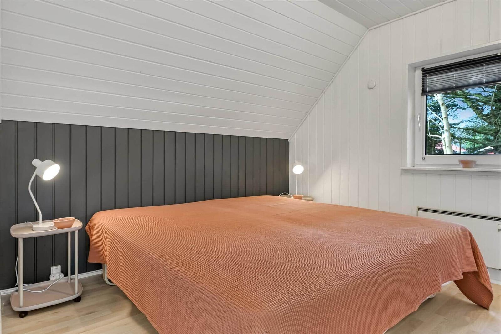 Schlafzimmer mit Bett, Nachttisch und Fenster. Wände weiß, Kopfteil dunkel.
