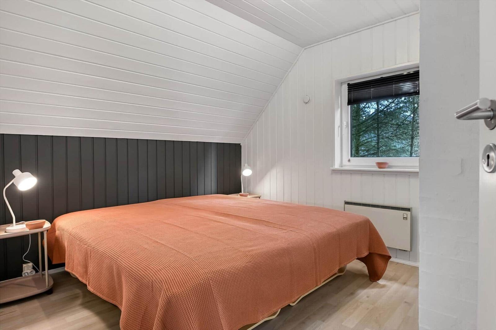 Schlafzimmer mit Bett, zwei Nachttischen und Fenster mit Blick auf Bäume.