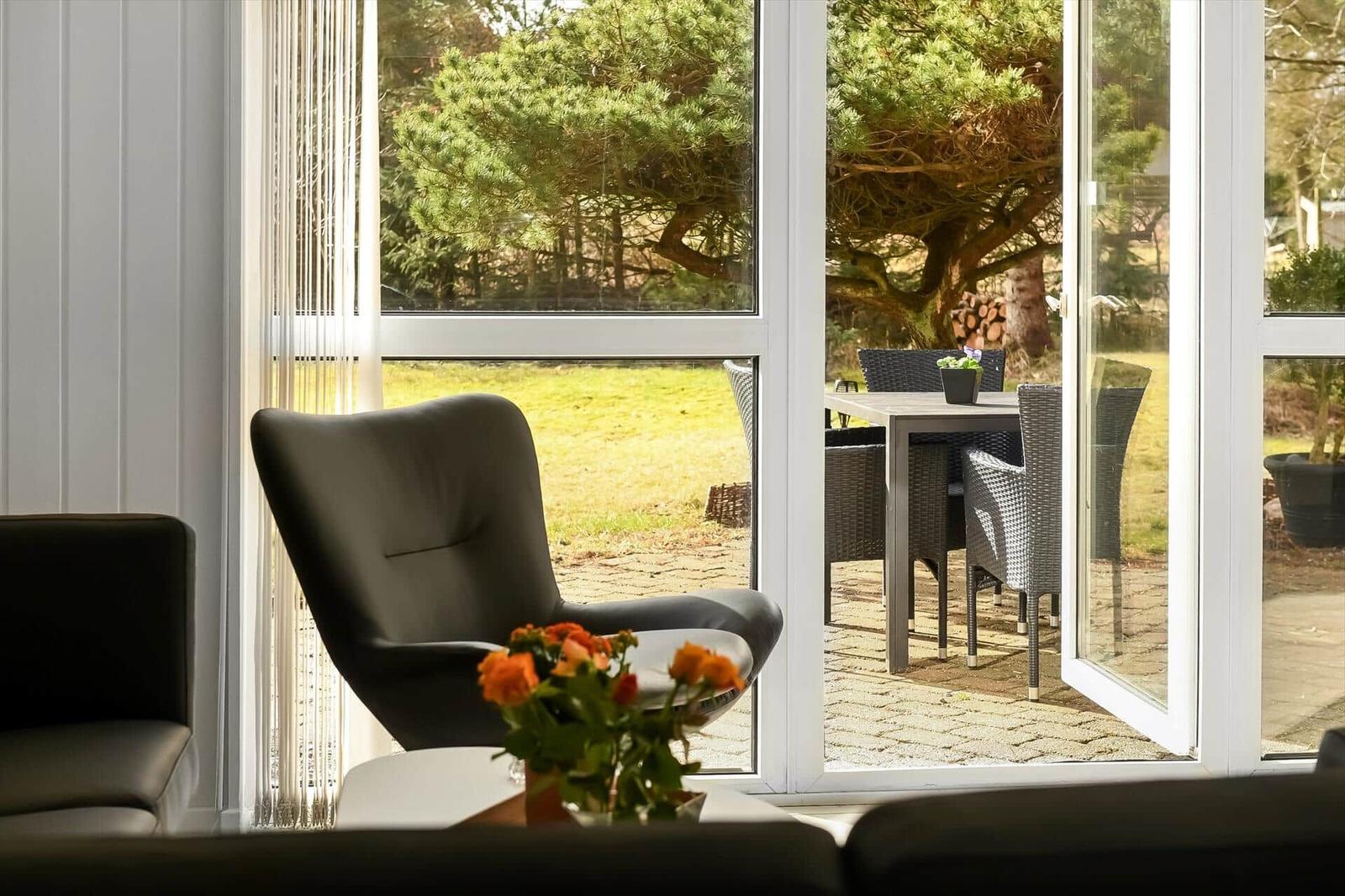 Ein schwarzer Sessel vor einem Fenster mit Blick auf eine Terrasse und Bäume.