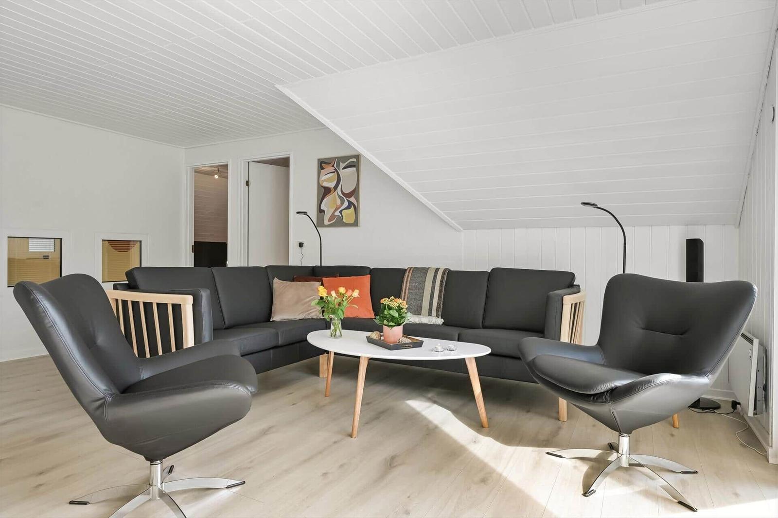 Wohnzimmer mit grauem Sofa, zwei schwarzen Sesseln und weißem Tisch.