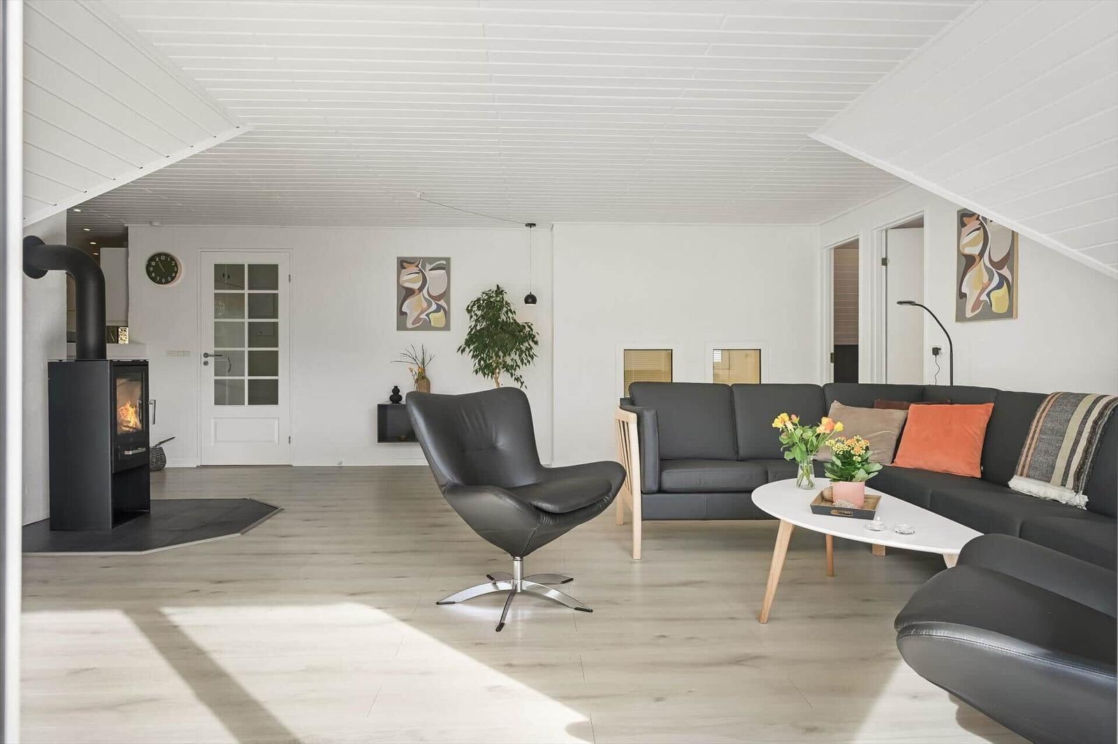 Wohnzimmer mit Sofa, Sessel und Kaminofen. Holzboden und weiße Wände.