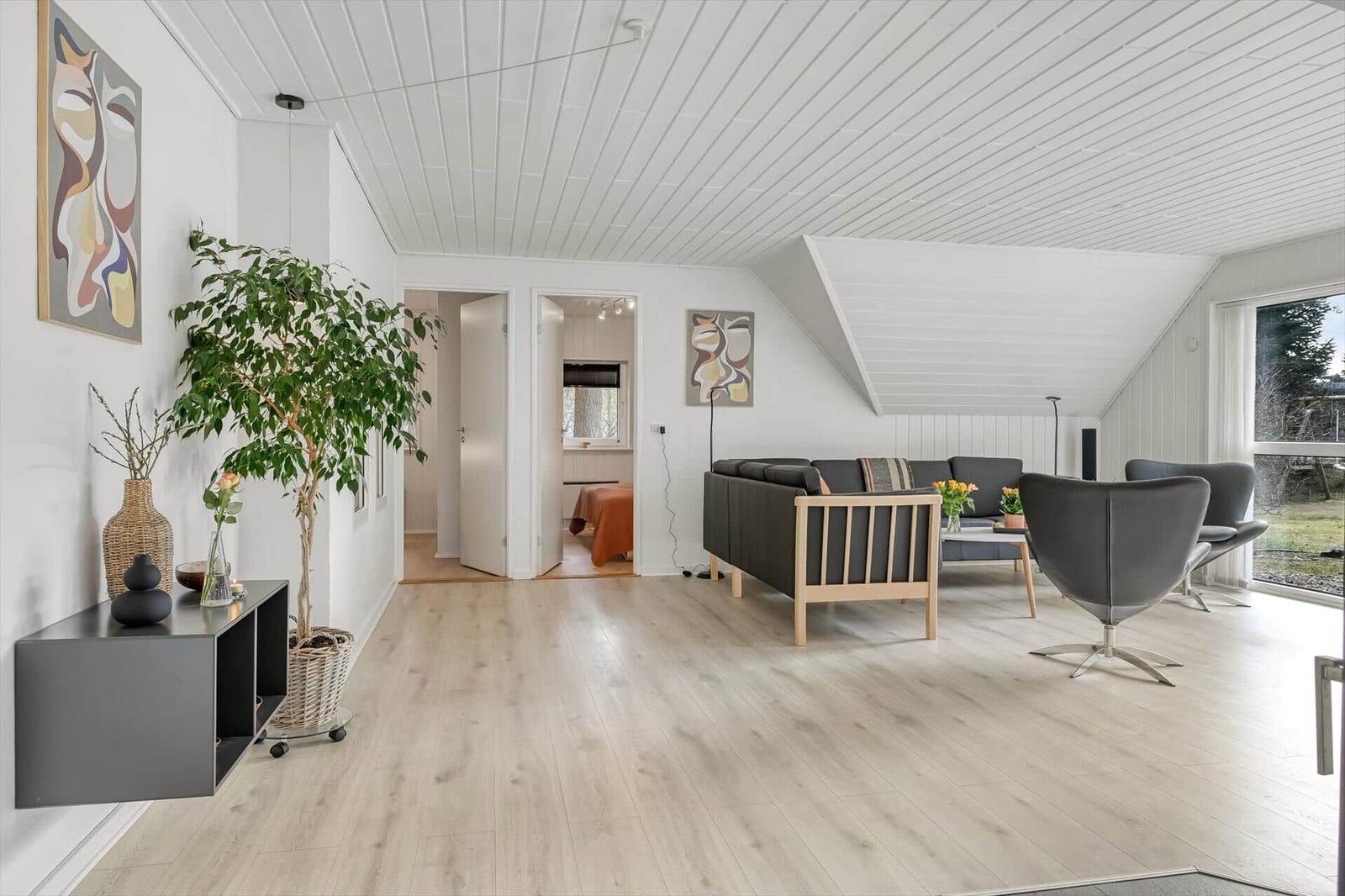 Wohnzimmer mit Sofa, Sessel und Holzboden. Blick auf Schlafzimmer und Garten.