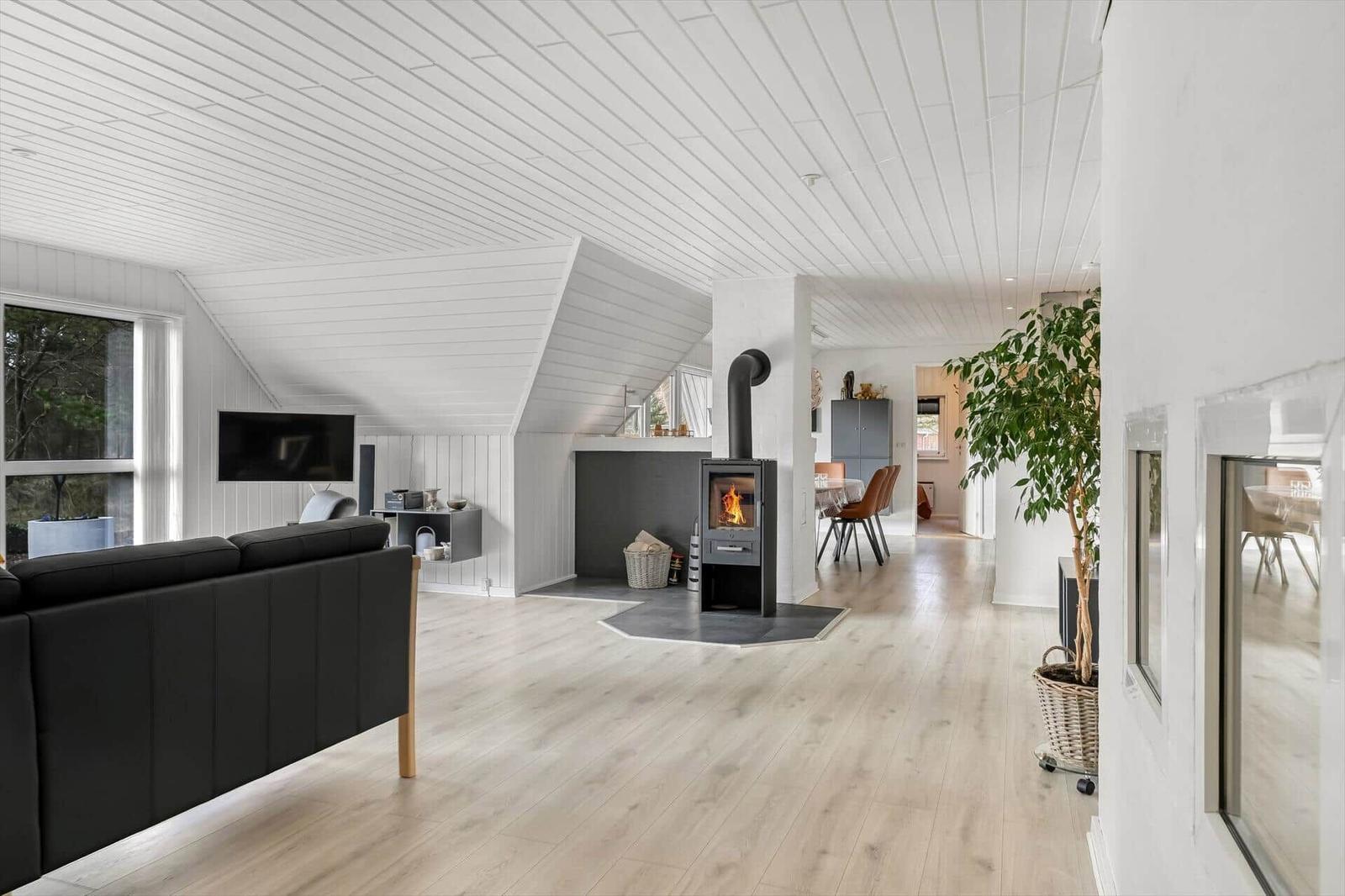 Wohnraum mit Kaminofen, Sofa und Holzboden. Blick in die Küche.