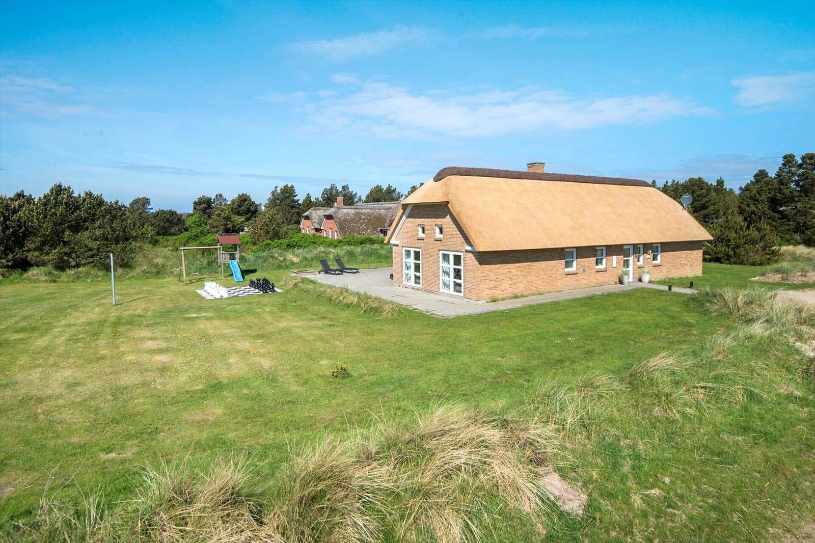 Ein Ferienhaus mit strohgedecktem Dach und großem Garten mit Spielplatz.
