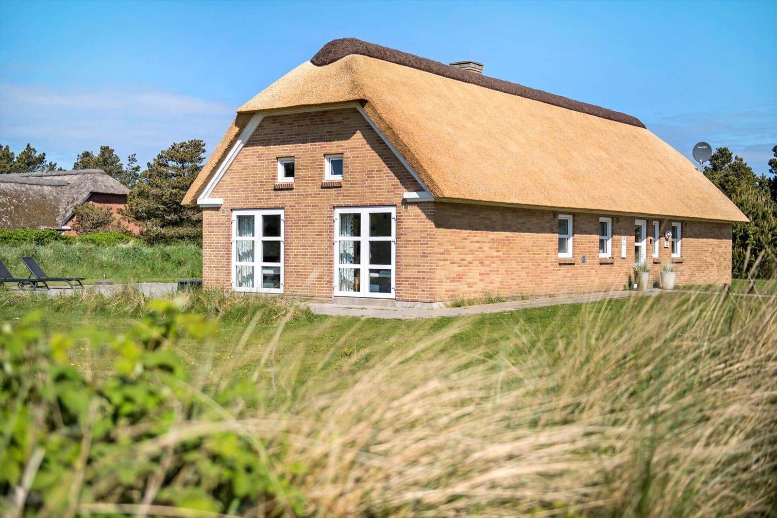 Ein Ferienhaus mit Strohdach und Backsteinfassade in einer grünen Umgebung.