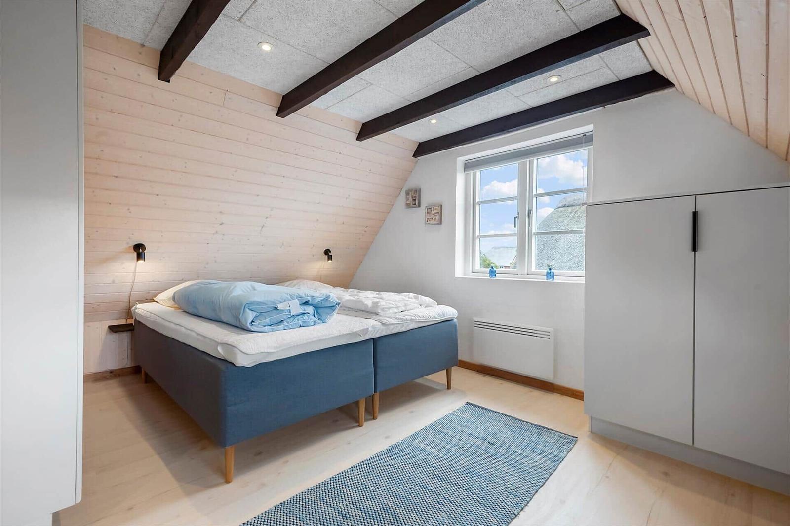 Schlafzimmer mit Bett, Kleiderschrank und Fenster. Holzwände und Deckenbalken.