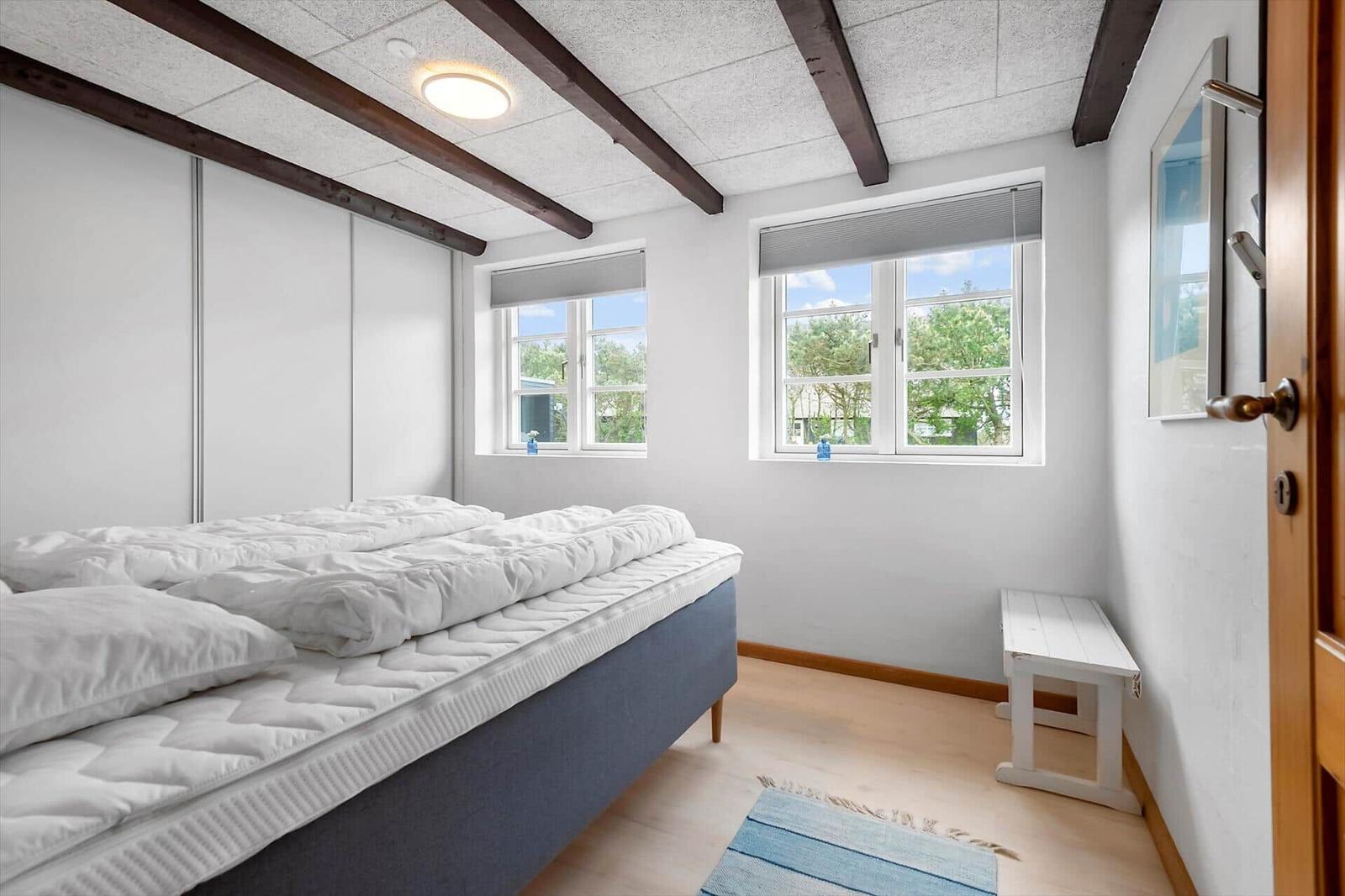 Schlafzimmer mit Bett, Fenstern und Holzbalken an der Decke.