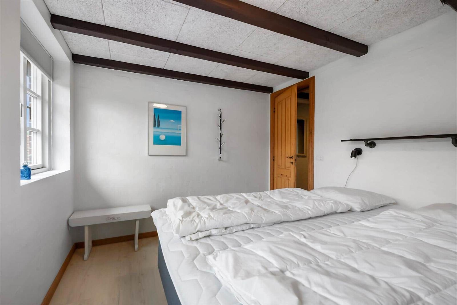 Schlafzimmer mit Bett, Fenster, Wandbild und Holztür.