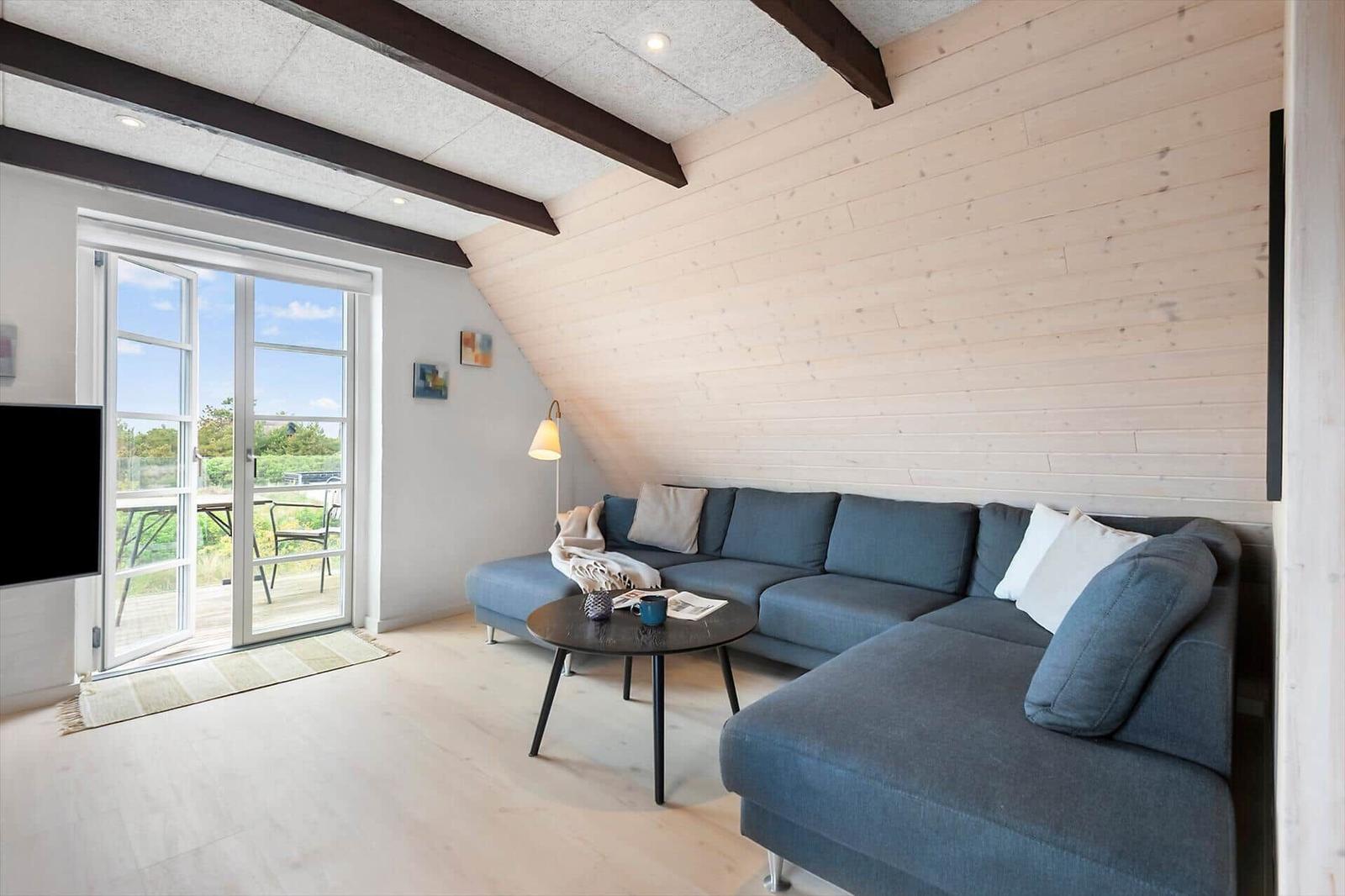 Ein Wohnzimmer mit blauem Sofa, Holzwand und Balkontür.