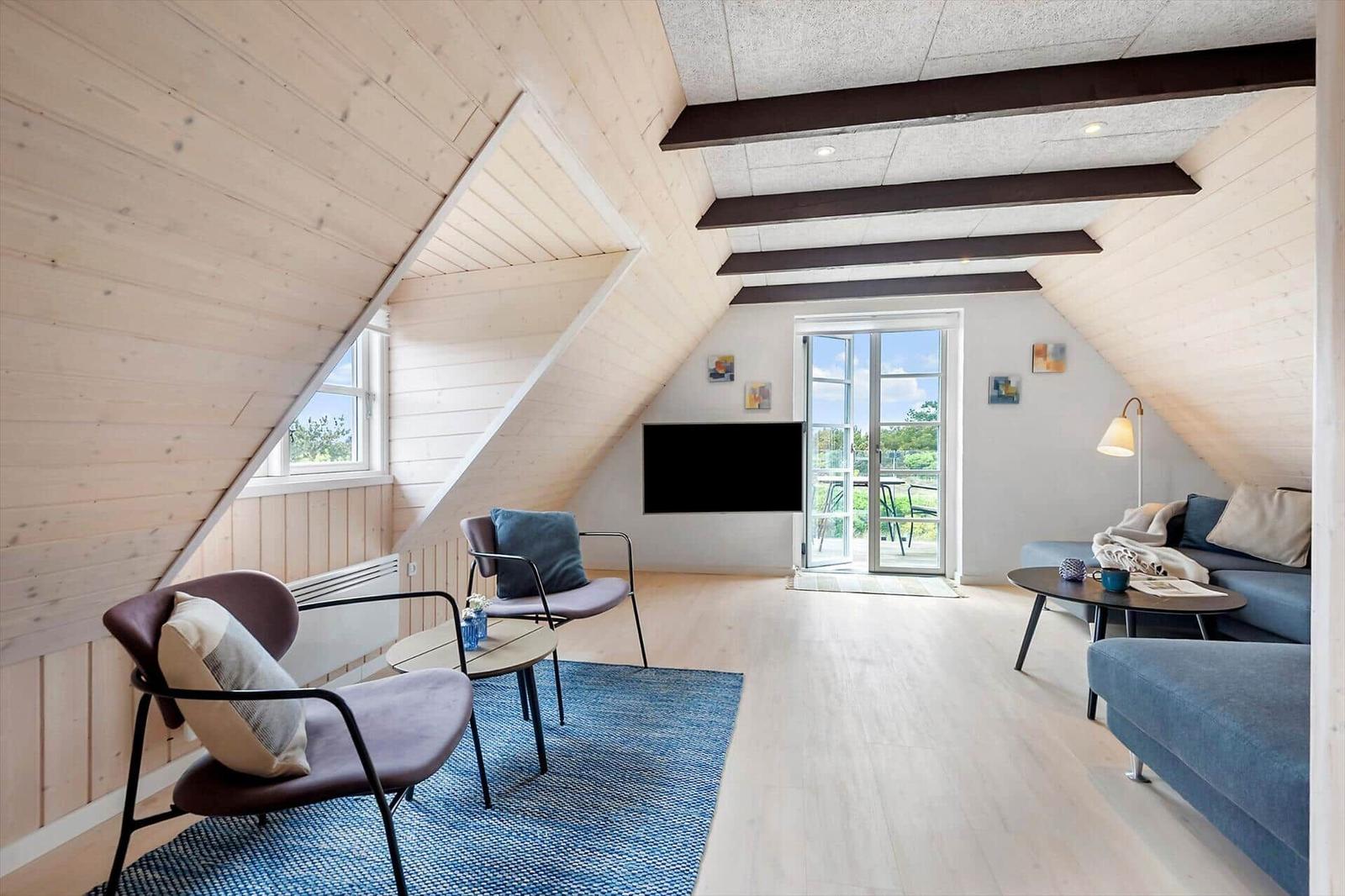 Wohnzimmer mit Holzwand, Sofa, Sessel und TV. Terrassentür führt nach draußen.