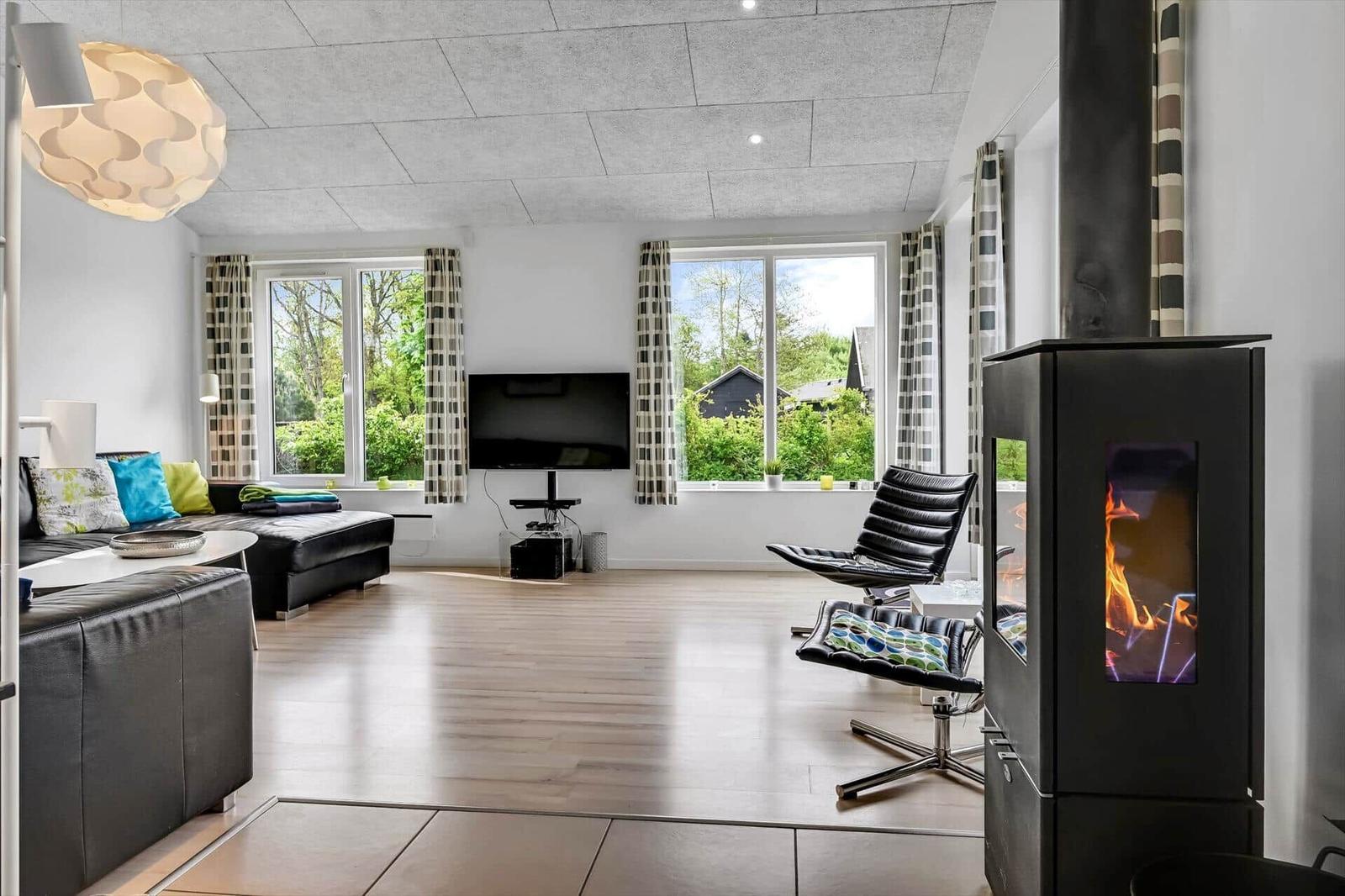 Wohnzimmer mit Kamin, Sofa, Fernseher und Fenstern mit Blick auf Grünflächen.